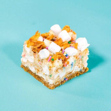 Cereal Milk Rocky Road square with crunchy cornflakes, marshmallows, caramelized white chocolate, and rainbow sprinkles.